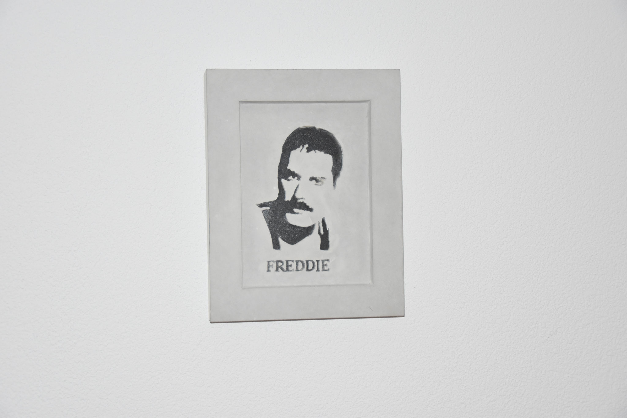 Betonportrait von Freddie Mercury mit markanter Silhouette und seinem Namen darunter, eingerahmt von einem minimalistischen Betonrahmen.